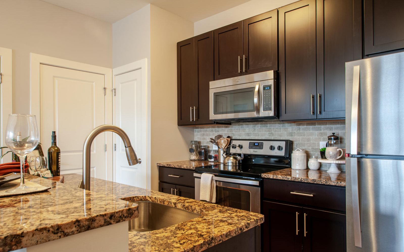 Modern kitchen with dark cabinets, stainless steel appliances, and a granite countertop island with a sink.