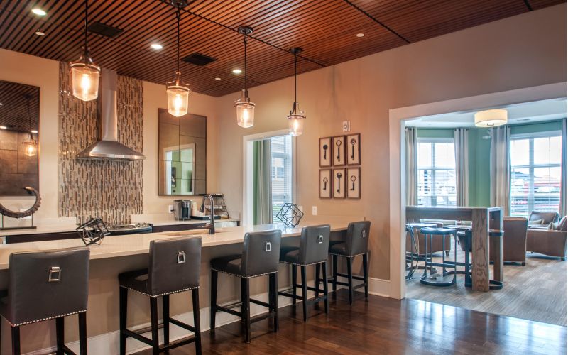 Modern kitchen with pendant lights, bar stools, wood floors, and a view into a cozy living area with large windows.