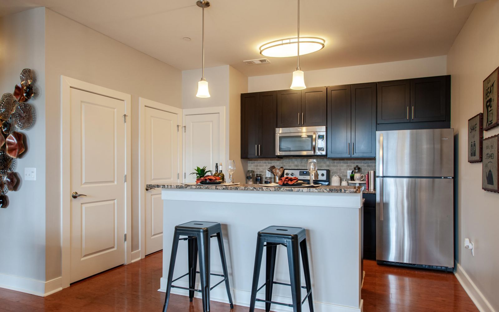 Modern kitchen with dark cabinets, stainless steel appliances, and two black barstools at a breakfast bar.