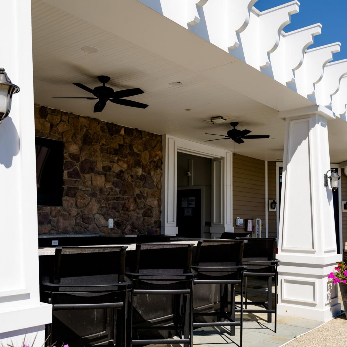 Outdoor bar seating under a white pergola with stone accents and two ceiling fans.