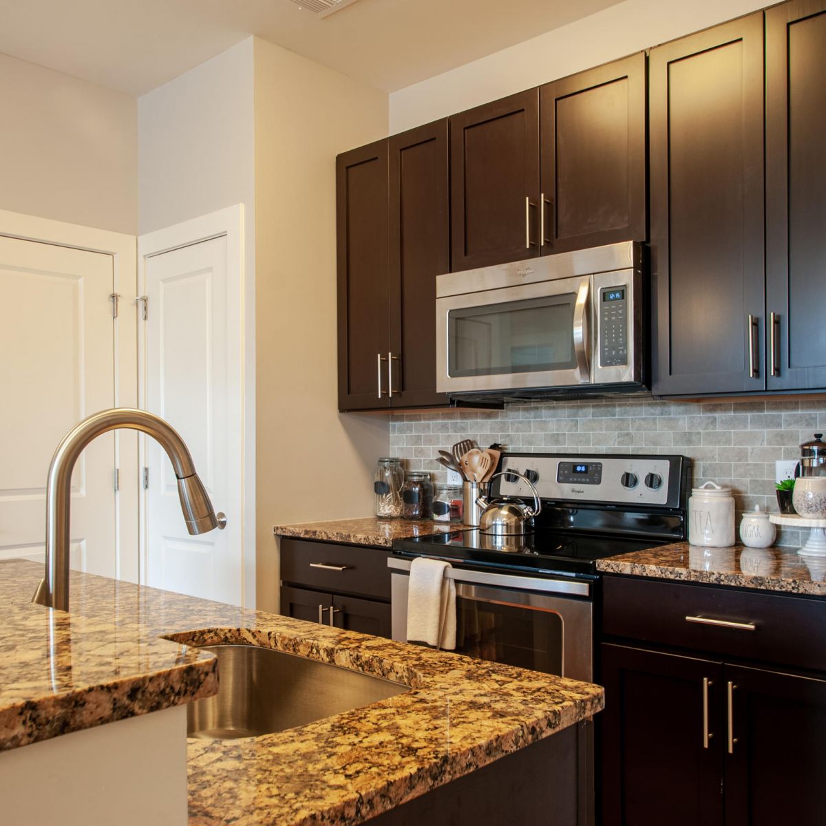 Modern kitchen with dark cabinets, stainless steel appliances, and a granite countertop island with a sink.